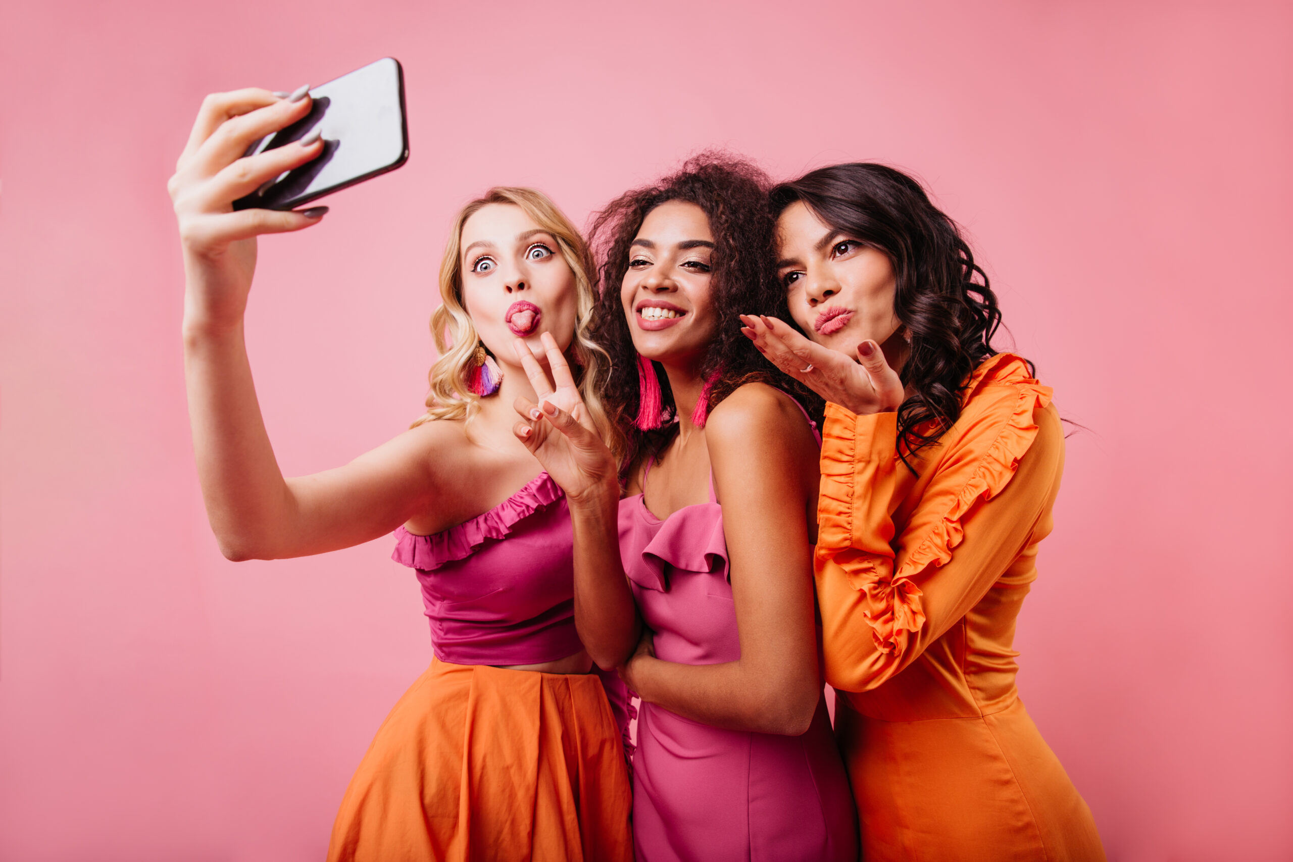 Latin happy girl sending air kiss. Charming ladies making selfie on pink background